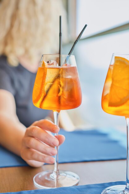 Blurred background adult woman holding an Aperol Spritz cocktail lunch in a cafe selective focus weekend at the sea Vertical shot