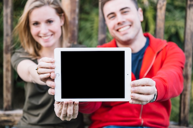 Blurred couple showing tablet near fence