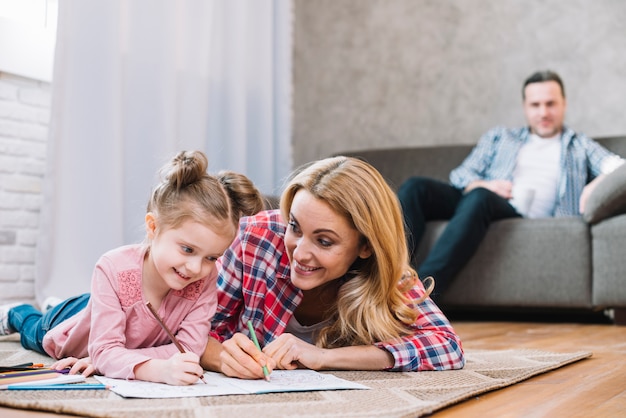 Blurred focus father looking their wife and daughter while drawing on book