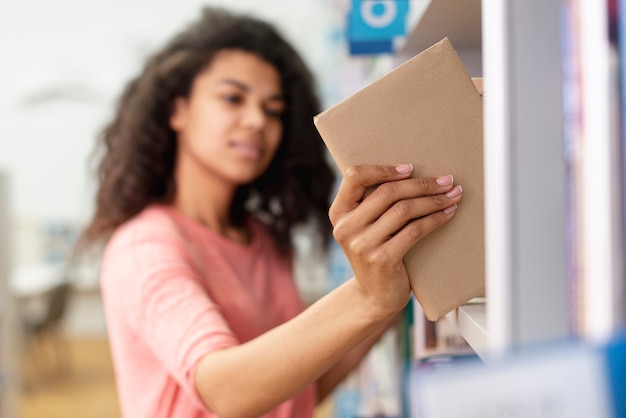 Ragazza vaga che mette libro sullo scaffale per libri