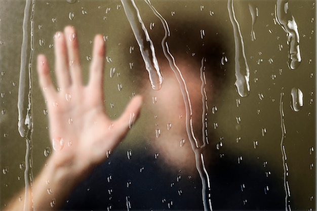 Uomo sfocato dietro la finestra con gocce di pioggia