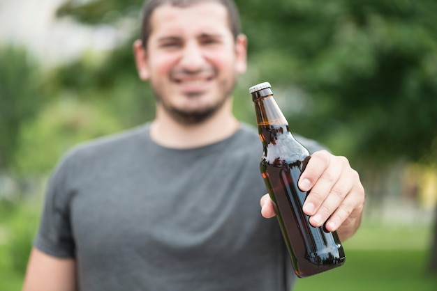 Foto gratuita uomo vago che mostra bottiglia di birra nel parco