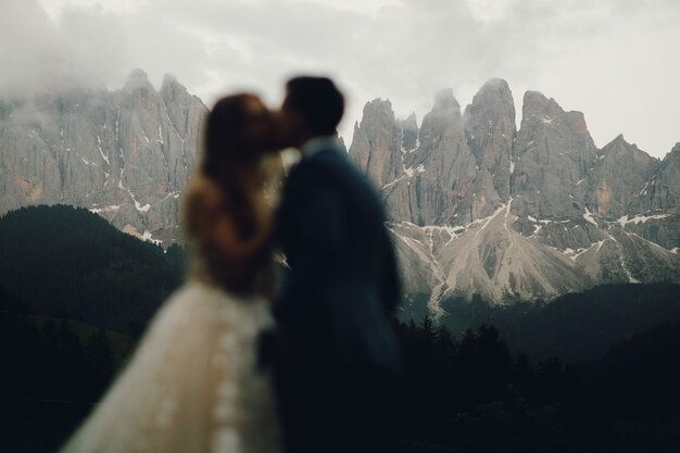 Blurred picture of kissing wedding couple standing before gorgeous mountain landscape 