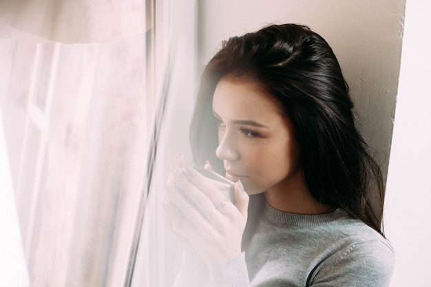 窓の上でお茶を飲む若い女性のぼかしの写真