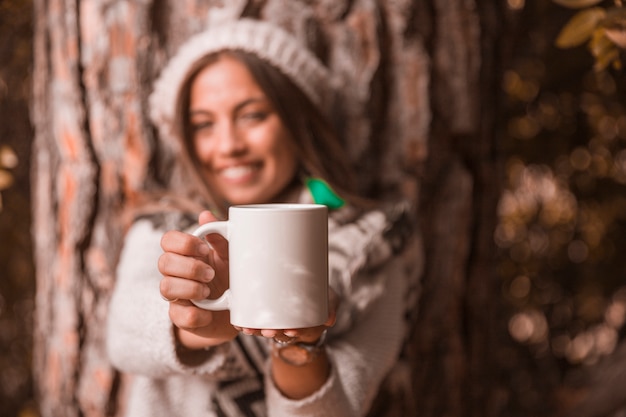 Foto gratuita donna vaga che mostra tazza vicino all'albero