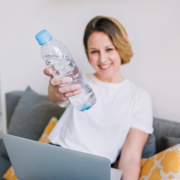 Размытые женщина с ноутбуком, показывая бутылку с водой