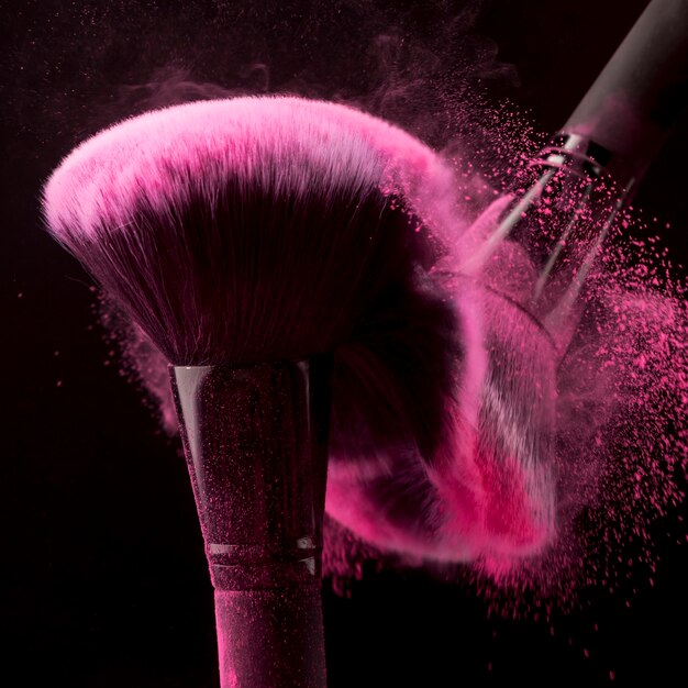 Blusher brushes scattering pink powder on black background