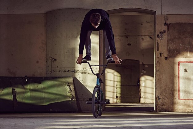 BMX rider doing stunts with a bicycle in a squat place.