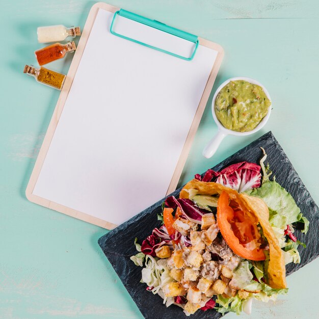 Board with dish and guacamole near clipboard