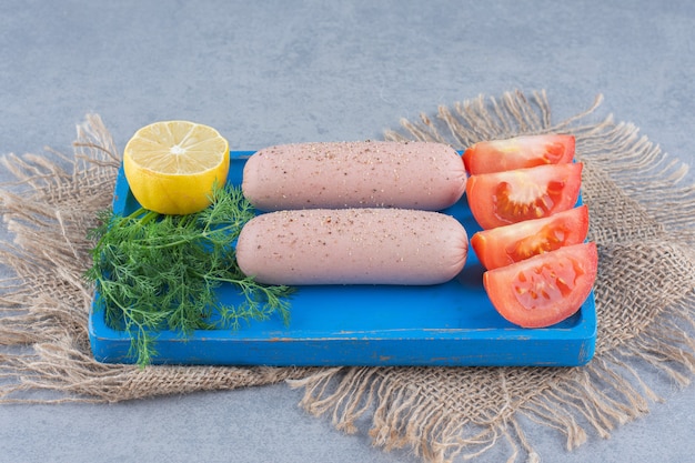 Free photo board with tasty sausages, tomato and lemon on wooden board.