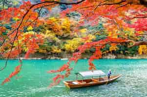 Бесплатное фото Лодочник плывет на лодке по реке. арасияма в осенний сезон вдоль реки в киото, япония