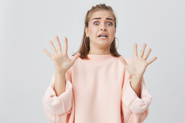 Body language. Disgusted stressed angry pretty girl with straight fair hair posing, keeping hands in stop gesture, trying to protect herself as if saying:Keep it away from me