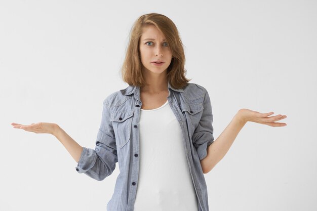 Body language. Emotional indignant young casually dressed female shrugging shoulders, being at loss, expressing indifference, having clueless confused expression, saying: Who cares? I don't know