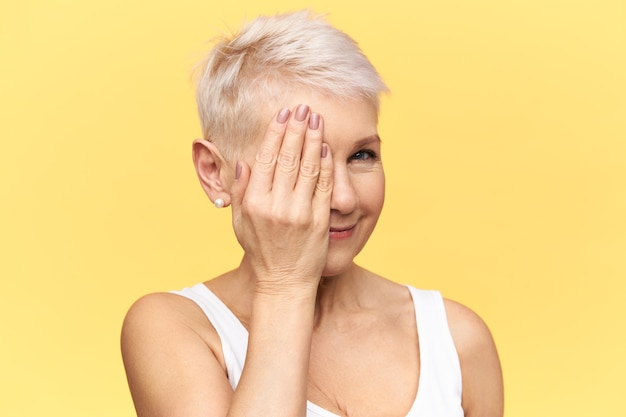 Free photo body language. portrait of attractive middle aged woman covering one eye with hand, having her vision being checked at ophthalmologist.