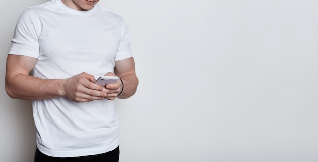 A body of muscular boy wearing white t-shirt holding smartphone typing a message communicating with people online