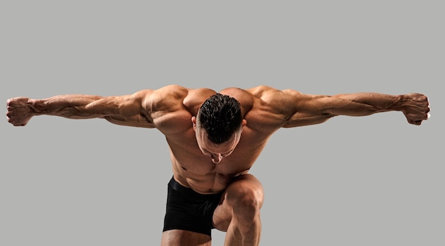 Bodybuilder posing  in studio, standing on knee.