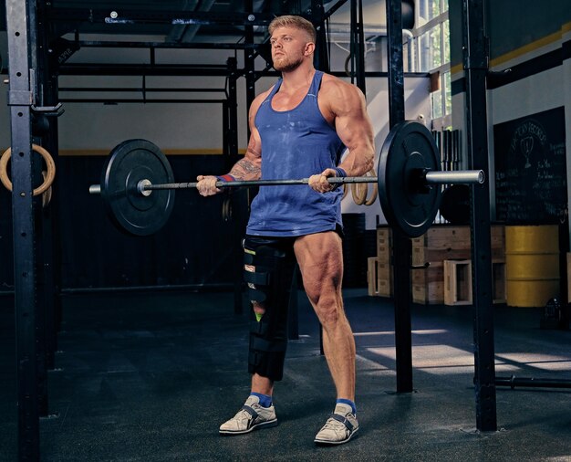 Bodybuilder with broken leg in bandage doing biceps workout with barbell.