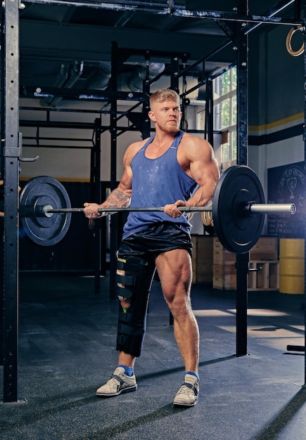 Bodybuilder with broken leg in bandage doing biceps workout with barbell.