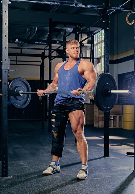 Bodybuilder with broken leg in bandage doing biceps workout with barbell.