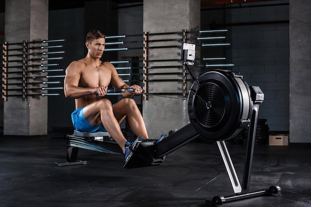 Free photo bodybuilder working on his legs with weight machine at the gym. muscular young man in blue shorts doing exercises.