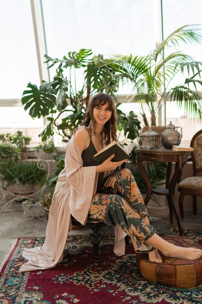 Bohemian woman in elegant home wear reading book in stylish living room.