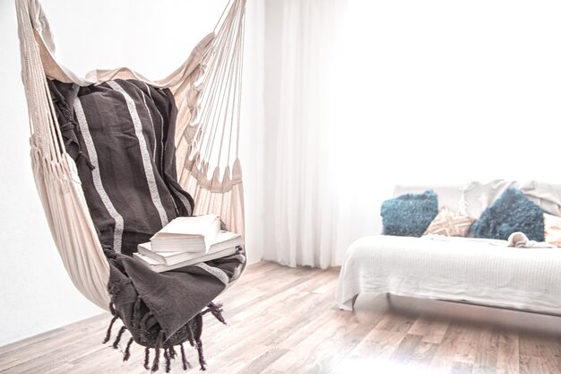 A boho-style hammock chair with a stack of books. Cozy interior. The concept of rest and home comfort. Space for text.