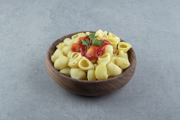 Boiled conchiglie pasta with ketchup in wooden bowl.