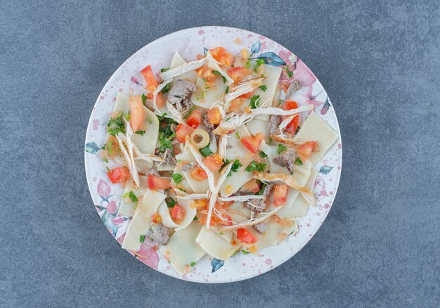 Boiled dough with chopped vegetables on colorful plate. 
