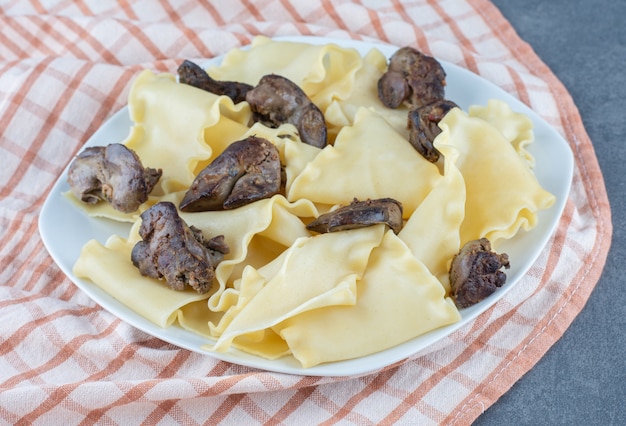 Pasta bollita con parti di carne secca sul piatto bianco.