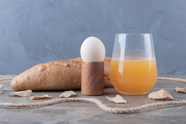 Boiled egg, bread and glass of juice on marble table. 