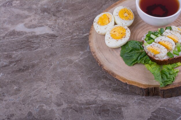 Boiled egg sandwich with a cup of tea on a wooden board.