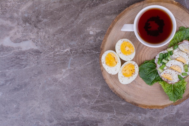 Boiled egg sandwich with a cup of tea on a wooden board.