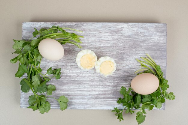 Boiled egg with uncooked egg on wooden cutting board.