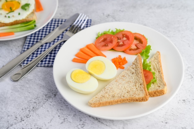 ゆで卵、パン、ニンジン、トマトを白い皿にナイフとフォークで。