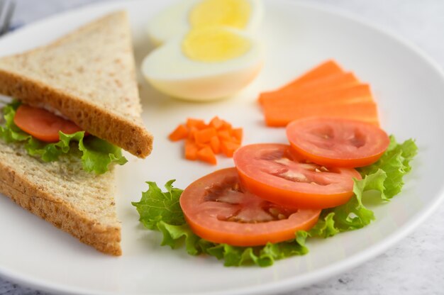Вареные яйца, хлеб, морковь и помидоры на белой тарелке с ножом и вилкой.