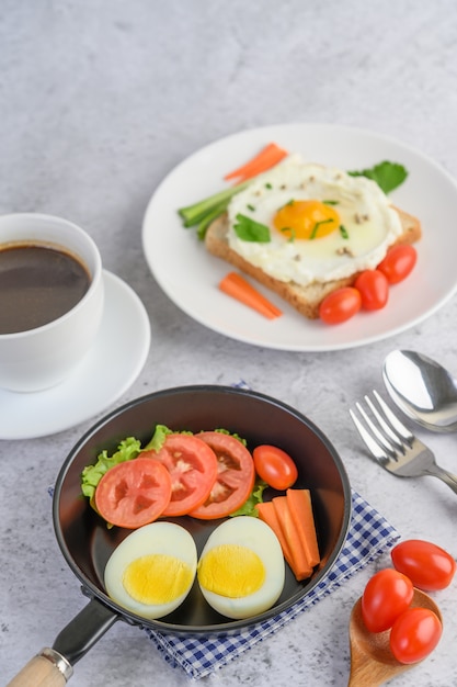 Boiled eggs, carrots, and tomatoes on a pan with tomato on a wooden spoon and coffee cup.