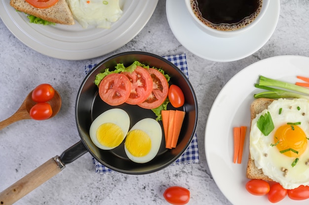 Boiled eggs, carrots, and tomatoes on a pan with tomato on a wooden spoon and coffee cup.