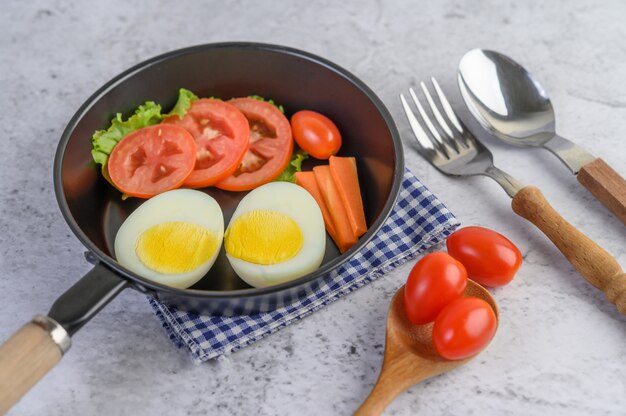 Boiled eggs, carrots, and tomatoes on a pan with tomato on a wooden spoon.
