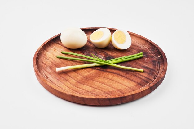 Вареные яйца и зеленый лук на деревянном блюде.