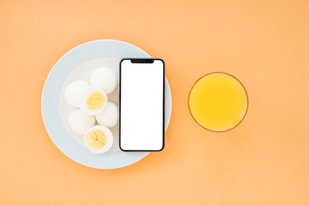 Free photo boiled eggs and mobile phone on white plate with orange juice glass on brown pale background