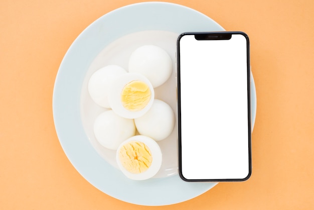 Free photo boiled eggs and mobile phone with white screen display smartphone on ceramic white plate