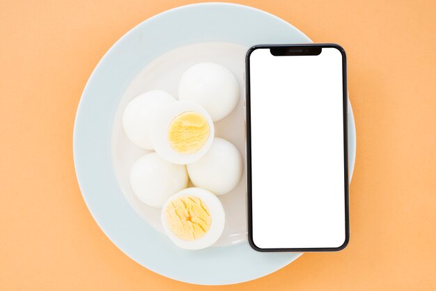 Вареные яйца и мобильный телефон с белым экраном дисплея смартфона на керамической белой тарелке