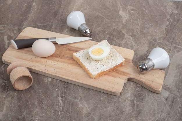 Вареные яйца и тосты на разделочной доске с ножом и специями. Фото высокого качества