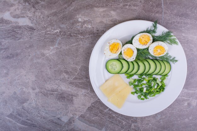 Boiled eggs with minced herbs and cucumbers in a white plate