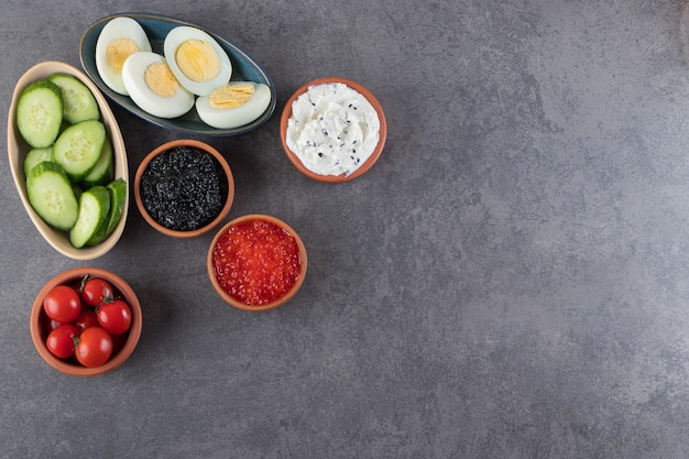 Boiled eggs with sausages and sliced cucumbers placed on stone background .