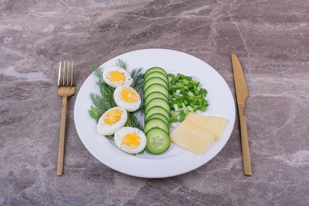Вареные яйца с нарезанными огурцами и зеленью в белой тарелке.