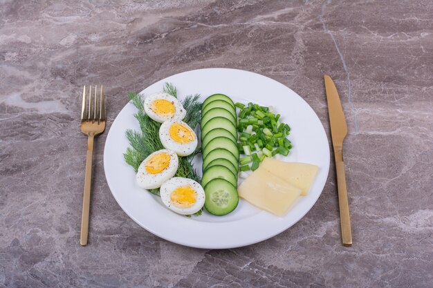 Boiled eggs with sliced cucumbers and herbs in a white plate.