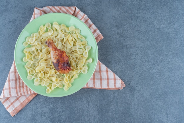 Free photo boiled macaroni and chicken leg on green plate.