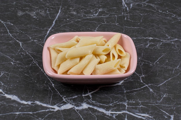 Boiled pasta in pink bowl over black.