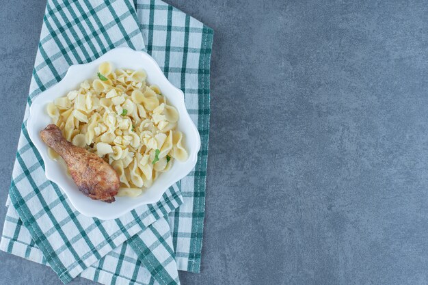 Boiled pasta with chicken drumstick in white bowl.